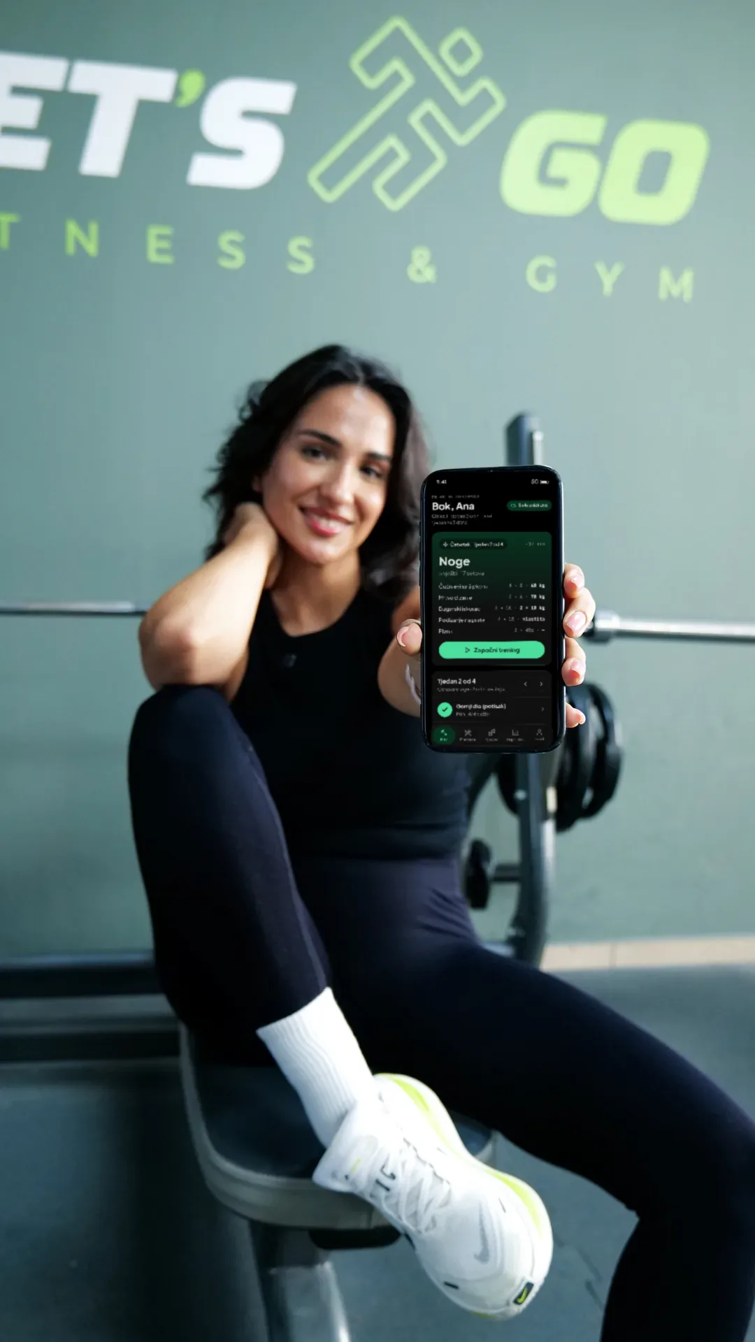 Korisnica u teretani LET'S GO Fitness & Gym drži telefon s otvorenim ekranom plana treninga