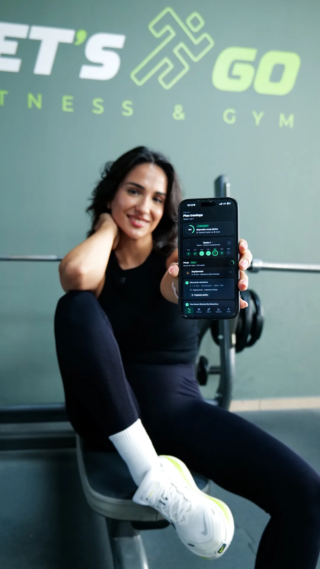 Korisnica u teretani LET'S GO Fitness & Gym drži telefon s otvorenim ekranom plana treninga
